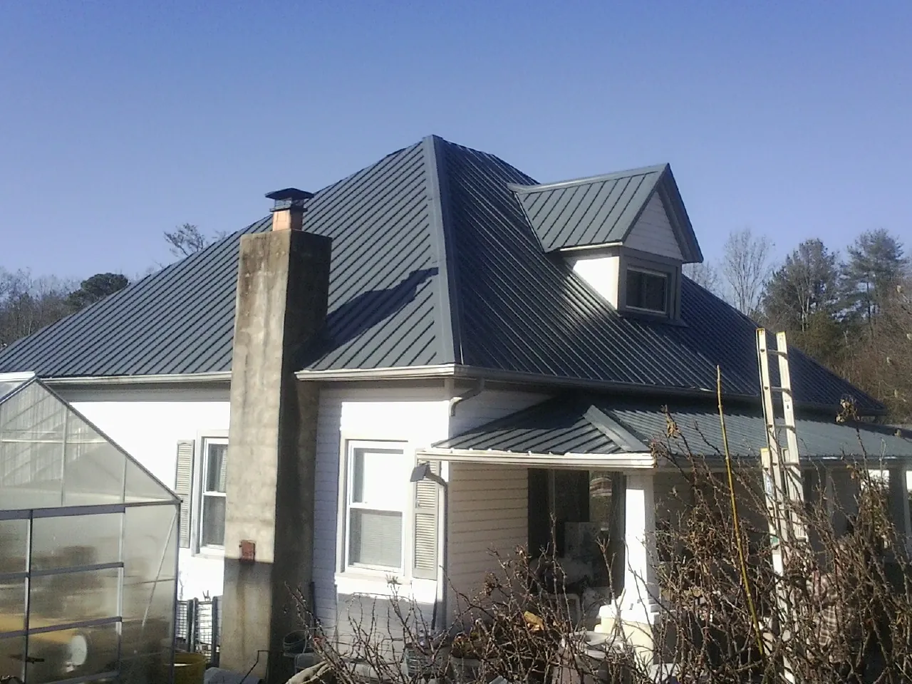 Dark blue standing seam metal roof on a white farmhouse with dormer — Slate & Tile Roof Repair by Roofing Brothers in Sunbury