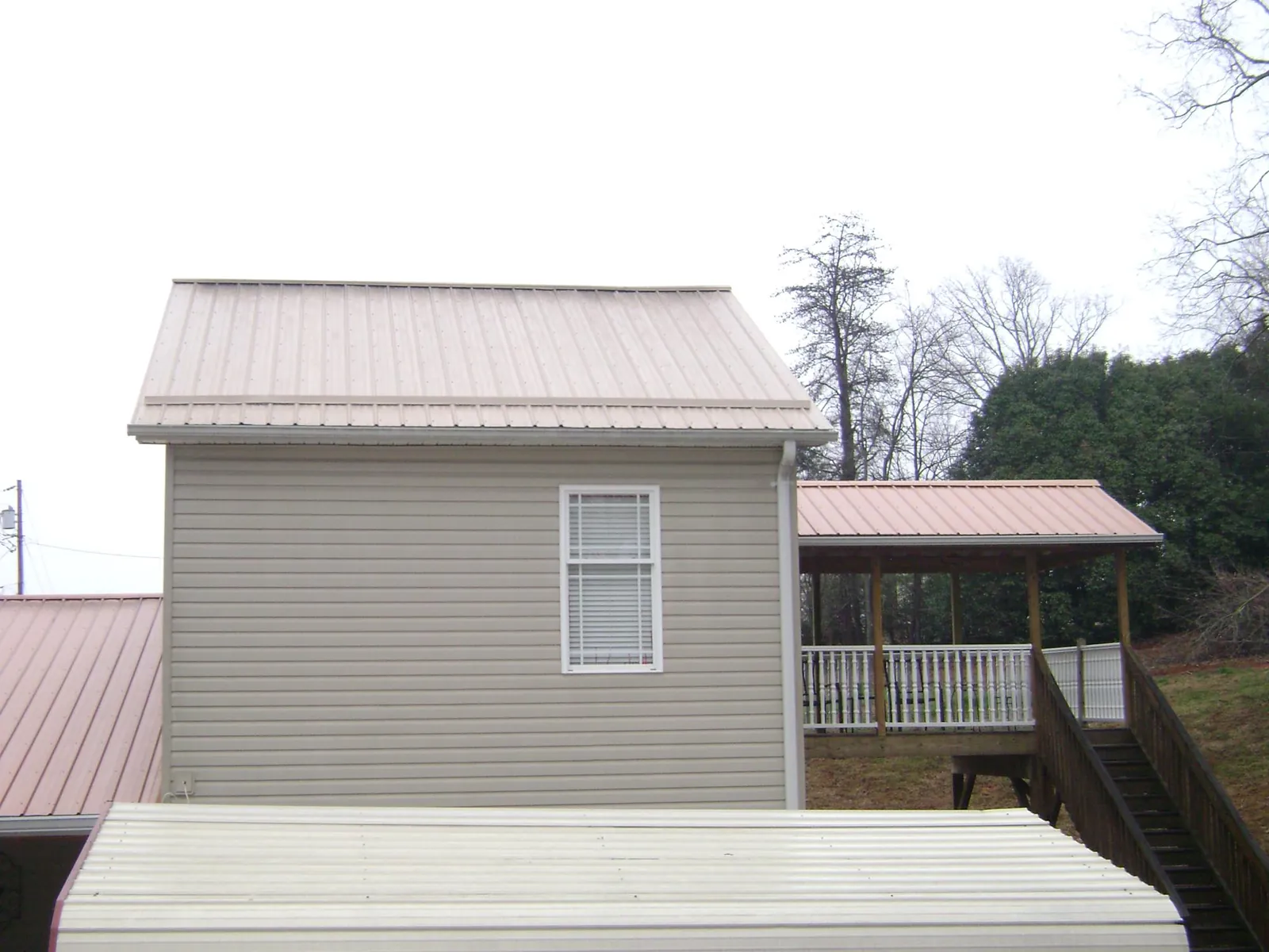 Tan metal roofs on a two story addition and attached porch, from a Roof Replacement job in Sunbury